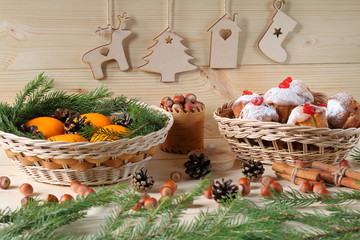 Obraz na płótnie Canvas Christmas and New Year composition. Composition of Christmas and New Year decorations from plywood, a wicker baskets with muffins and tangerines, nuts and fir branches on a wooden background.