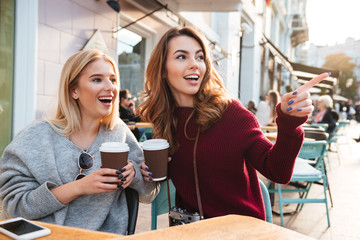 Two excited smiling girls holding coffee cups