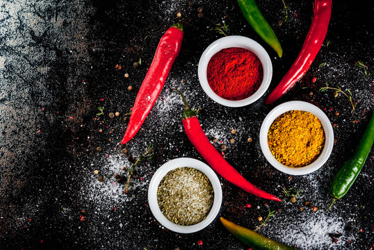 Various spices and seasonings. Cooking background.  Turmeric, curry, paprika, pepper, chili, dried basil, salt, fresh chili, thyme. Black rusty metal background. Top view, copy space.