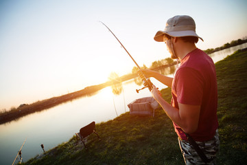 Young man fishing on a lake at sunset and enjoying hobby