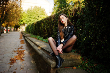 Stylish brunette girl wear on leather jacket and shorts sitting at street of autumn city.