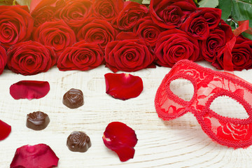 Red carnival mask and lipstick on a wooden table, scarlet roses on a background