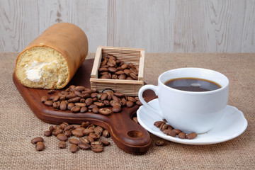 Roll coffee cake , a cup of coffee and coffee bean on wooden cutting board