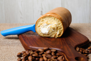 Roll coffee cake with knife and coffee bean on wooden cutting board