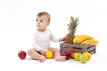 Fototapeta premium looking at fruit cute smiling baby on white background among fruits. Photo with depth of field