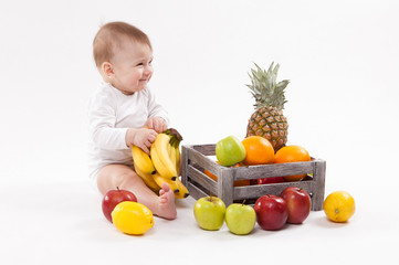 Fototapeta na wymiar looking at fruit cute smiling baby on white background among fruits. Photo with depth of field