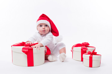 beautiful kid sitting in a New Year's cap and white body among the boxes of Christmas gifts and looking at the camera