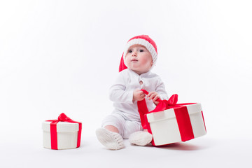 beautiful kid sitting in a New Year's cap and white body among Christmas boxes with gifts and unpacks gift