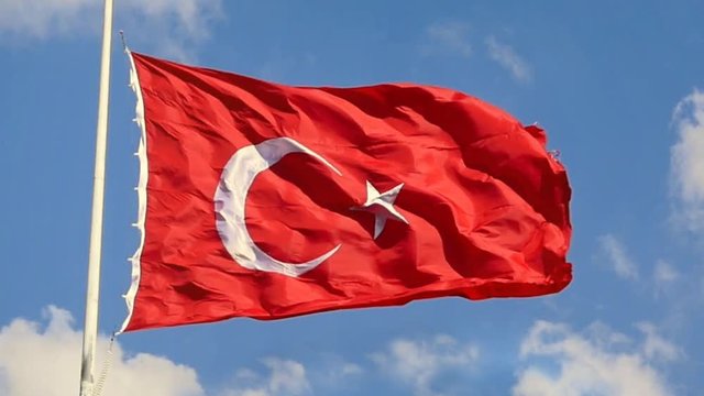Slow Motion, Zoom Out. Turkish Flag waving in the wind over blue sky with white clouds. The flag of Turkey; A red flag featuring a white star and crescent often called as moon-star (Ayyildiz)
