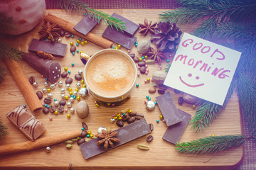 Hot coffee and christmas decorations . Cup of coffee and chocolate on wooden table. Christmas decorations on a kitchen, gifts and food on a wooden background. Magic moments in everyday life