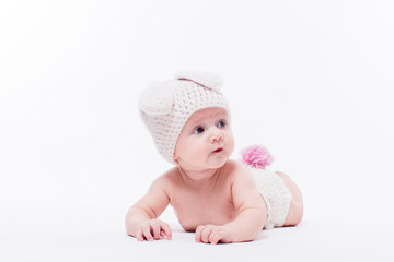 Cute baby girl lying naked on a white background wearing a hat in the form of a Christmas bunny with pink ears and tail