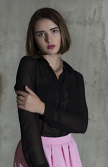 Woman in her black long sleeved shirt and pink skirt. Half-lenth. Grey grange wall background.