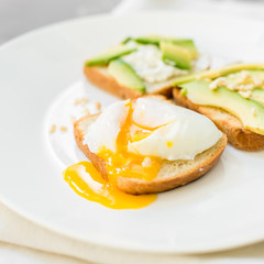 Breakfast. Eggs on toast with avocado, soft white cheese, spices and nuts. White plate, gray concrete background.