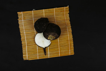 black radish with a cut on a bamboo mat, black background
