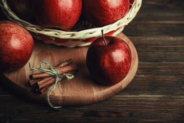 Autumn composition with fresh red apples and cinnamon in a wooden basket on rustic wooden background. Red apples and cinnamon