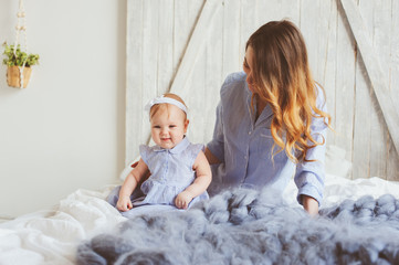 happy mother and 9 month old baby in matching pajamas playing in bedroom in the morning. Cozy family weekend.