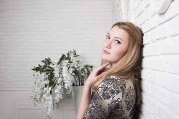 Fototapeta premium A beautiful girl is standing with her back against a white wall and smiling