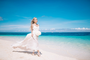 Fototapeta na wymiar Beautiful bride in long white dress on the beach with white bouquet