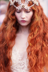 Beautiful red-haired girl with long curly hair in the bride, in a long lace dress. A natural beauty.