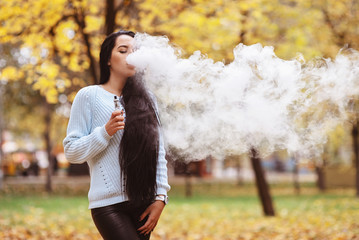 Vaping. Young beautiful woman vaping with smoke outdoors. Vapor concept.