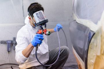 A varnisher is painting a bodywork of a car with a spray gun. No face but dust mask - obrazy, fototapety, plakaty