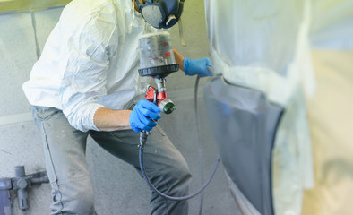 A varnisher is painting a bodywork of a car with a spray gun. No face but dust mask