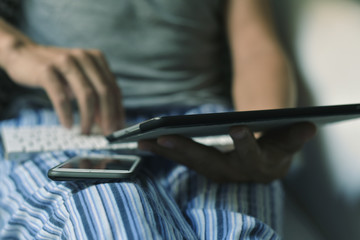 man in pajamas using a smartphone and a tablet