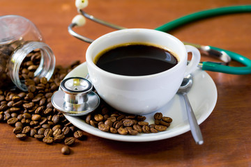Cup of dark coffee  with coffee beans and stethoscope on  wooden background. Health  concept of who like drink a coffee.
