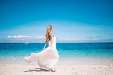 Fototapeta na wymiar Beautiful bride in long white dress running on the white sand beach .