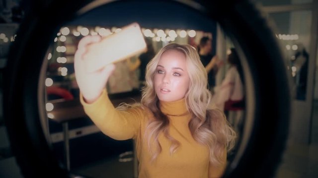 Blonde beautiful woman do selfie in make up room.
