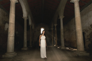 Fototapeta na wymiar Mujer con vestido blanco en el templo antiguo iluminada por la luz del sol al atardecer