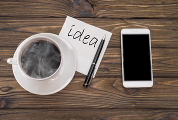 Inscription Idea on a napkin and cup of coffee on a tree background. phone