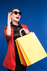 portrait of brunette girl in sunglasses with bags in the hands on a blue background