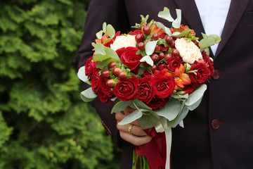 Wedding bouquet of red roses in the groom's hand on a green background