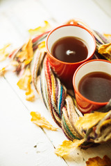 two red cups, wrapped in a scarf book and yellow leaves, autumn background, concept on the subject of comfort, warmth, pleasure, image toning