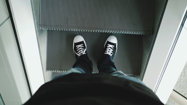 Closeup top view on man legs in sneakers traveler using moving escalator at airport terminal.