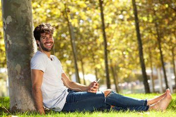 Naklejka na ściany i meble Happy man sitting in grass with cellphone and headphones