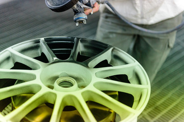 Close up of a varnisher is painting an alloy rim of a car with a spray gun. No face