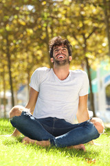 Portrait of handsome man sitting outside in grass leaning back laughing
