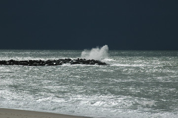 Dark skies in the background announce the arriving storm, the waves hitting the groynes are already harsh.