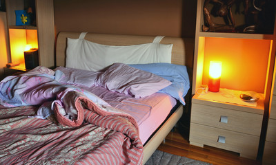 il letto disfatto al mattino quando ci si sveglia.  la camera da letto, le coperte, le lenzuola, le luci sul comodino