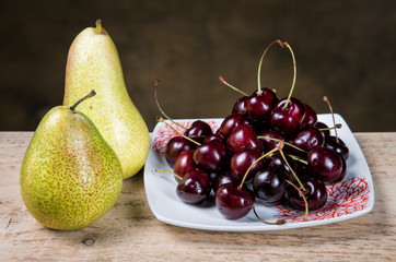 berries cherries in a plate and pears on a table