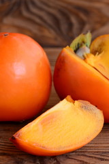 Ripe fresh persimmon on a brown wooden background. Slices persimmon photo. Tasty winter fruits. Source of beta carotene, dietary fiber and minerals. Closeup
