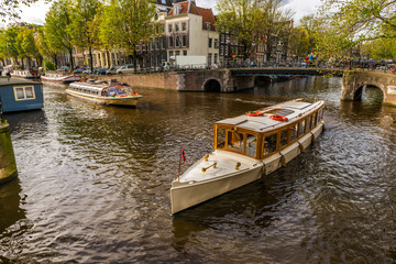 Fototapeta na wymiar Canal à Amsterdam et ses vedettes touristiques, Hollande aux Pays-Bas