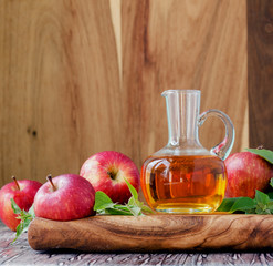 jug with apple cider vinegar and ripe red apples on wooden table, selective focus