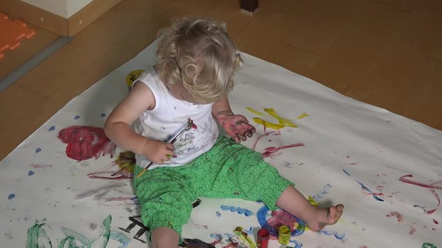 Lovely baby girl with colorful brush painting on herself clothes