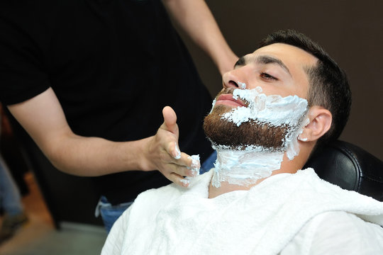 Barber preparing man face for shaving with hot towel on face in barber shop