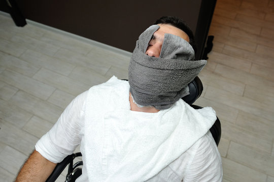 Barber Preparing Man Face For Shaving With Hot Towel On Face In Barber Shop