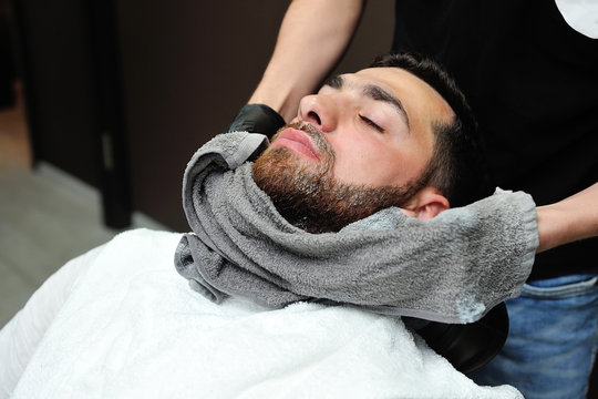 Barber preparing man face for shaving with hot towel on face in barber shop