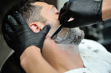 Hairdresser shaves man's beard with a blade in a male barber shop